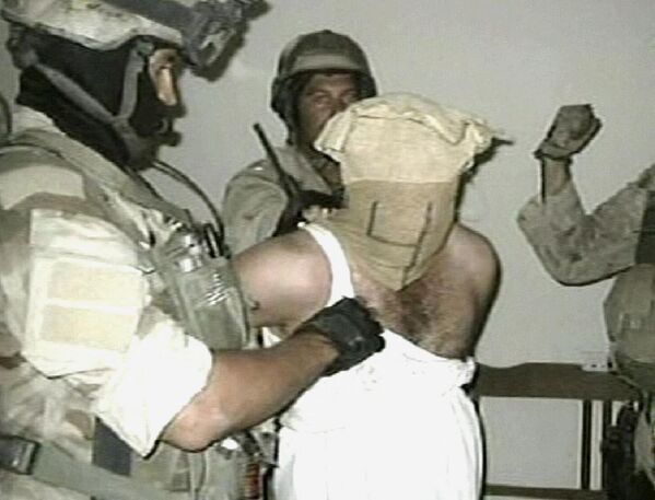 تظهر لقطة تلفزيونية مأخوذة من شبكة تلفزيون &quot;الجزيرة&quot; الإخبارية، في 4 ديسمبر/ كانون الأول 2004، صورة لسجين عراقي محتجز تحت تهديد السلاح. يُعتقد أن هذه الصورة والعديد من الصور الأخرى التي تم التقاطها في مايو/ أيار عام 2003، التي عثر عليها صحفي من وكالة &quot;أسوشيتد برس&quot; على موقع مشاركة صور عام، حيث ورد أن من شاركها هو زوجة جندي أمريكي عاد من الحرب. دولة. أفاد التلفزيون الأمريكي حينها أن الجيش الأمريكي يحقق في صور لإساءة معاملة سجناء عراقيين على ما يبدو التقطت قبل تلك الصور التي تظهر إساءة معاملة القوات الأمريكية لسجناء أبو غريب، الأمر الذي أثار فضيحة كبرى. - سبوتنيك عربي