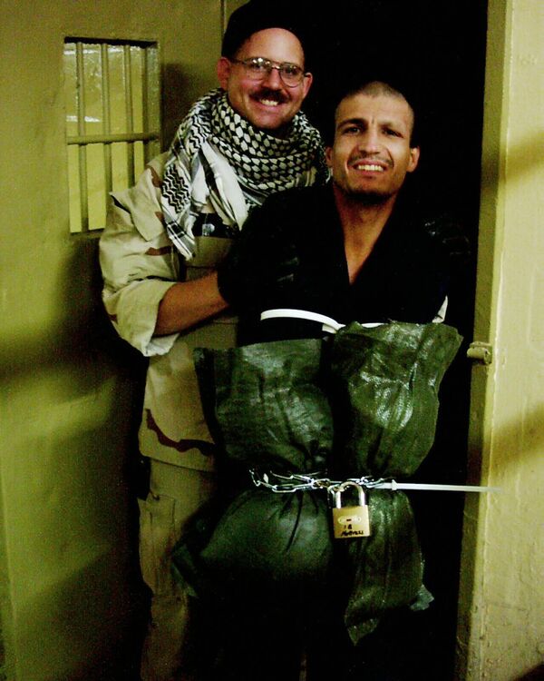 هذه صورة حصلت عليها وكالة &quot;أسوشيتد برس&quot; والتي تُظهر فيها الجندي تشارلز غرانر الابن يقف مع معتقل عراقي وُضعت ذراعيه في أكياس ورُبطت بأصفاد بلاستيكية وسلسلة مقفلة في سجن أبو غريب في بغداد، في أواخر عام 2003. - سبوتنيك عربي