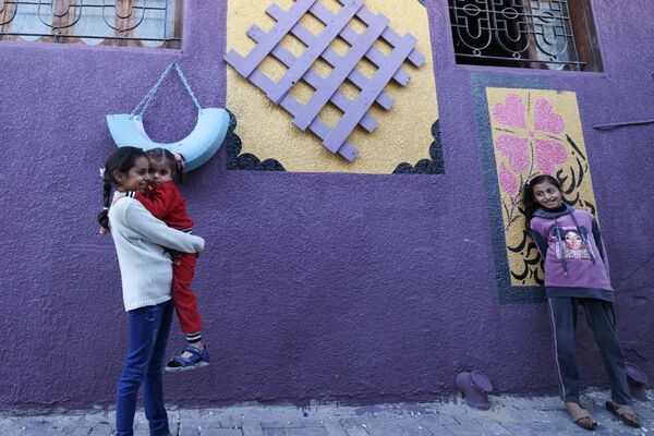 فتيات تقف على خلفية منزل رسم على جدرانه رسومات مختلفة كجزء من مبادرة لفنان فلسطيني، في حي الزيتون بمدينة غزة، قطاع غزة، فلسطين 12 مارس  2023. - سبوتنيك عربي