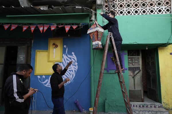 رجل يعلق فانوس رمضان على جدار مدهون بألوان زاهية كجزء من مبادرة لفنان فلسطيني، في حي الزيتون بمدينة غزة، قطاع غزة، فلسطين، 12 مارس 2023. - سبوتنيك عربي