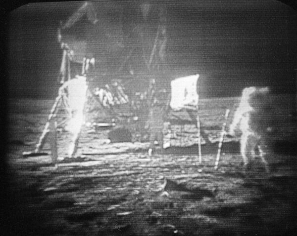 رائد فضاء &quot;أبولو -11&quot; نيل أرمسترونغ (يمين الصورة)، يسير على سطح القمر تاركًا وراءه آثار أقدام، 20 يوليو/ تموز 1969. يمكن رؤية العلم الأمريكي، الذي ثبته رواد الفضاء على السطح، بين أرمسترونغ والمركبة القمرية. إدوين ألدرين يُرى بالقرب من المركبة. أفاد رواد الفضاء بأن سطح القمر كان مثل الرمال الناعمة وتركوا آثار أقدام بعمق عدة بوصات أينما ساروا. - سبوتنيك عربي