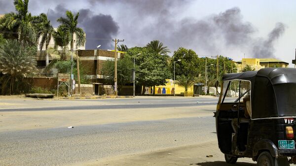 الدخان يتصاعد من المباني بينما يجلس سائق تاكسي التوكتوك في سيارته على طول شارع مهجور في الخرطوم في 16 أبريل 2023 ، أثناء القتال المستمر بين قوات اثنين من الجنرالات المتناحرين. - سبوتنيك عربي