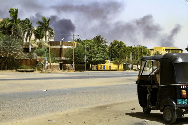 الدخان يتصاعد من المباني بينما يجلس سائق تاكسي التوكتوك في سيارته على طول شارع مهجور في الخرطوم في 16 أبريل 2023 ، أثناء القتال المستمر بين قوات اثنين من الجنرالات المتناحرين. - سبوتنيك عربي