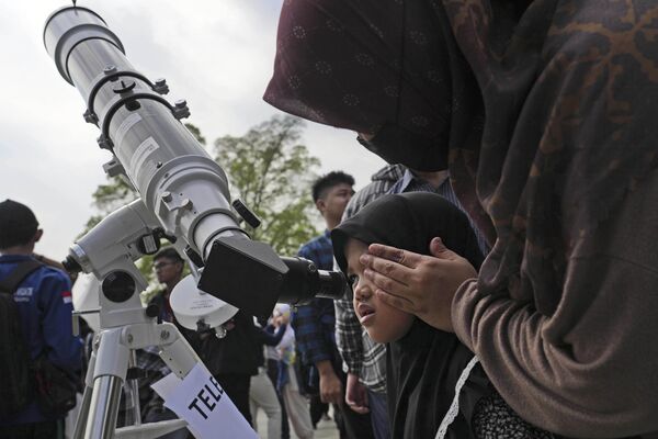امرأة تساعد ابنتها على مشاهدة كسوف الشمس من خلال التلسكوب في جاكرتا، إندونيسيا، 20 أبريل 2023.  - سبوتنيك عربي
