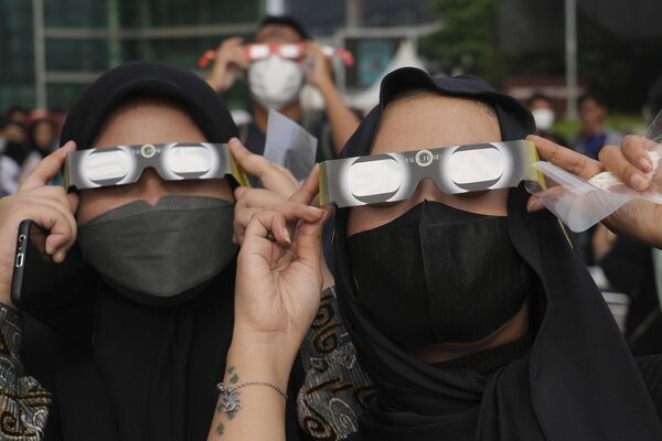 النساء الإندونيسيات يستخدمن نظارات واقية لمشاهدة كسوف الشمس في جاكرتا، إندونيسيا، الخميس 20 أبريل 2023.  - سبوتنيك عربي