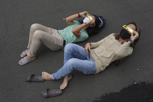 يرقد الناس على الأرض وهم يستخدمون نظارات واقية لمشاهدة كسوف الشمس في جاكرتا، إندونيسيا، 20 أبريل 2023.  - سبوتنيك عربي