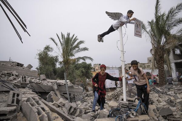 فتيات فلسطينيات يقفن بجانب تمثال يمثل طفلا فلسطينيا بجناحي ملاك، فوق أنقاض منزل دمر في التصعيد العسكري الأخير مع إسرائيل في دير البلح، وسط قطاع غزة، 8 يونيو 2023 - سبوتنيك عربي