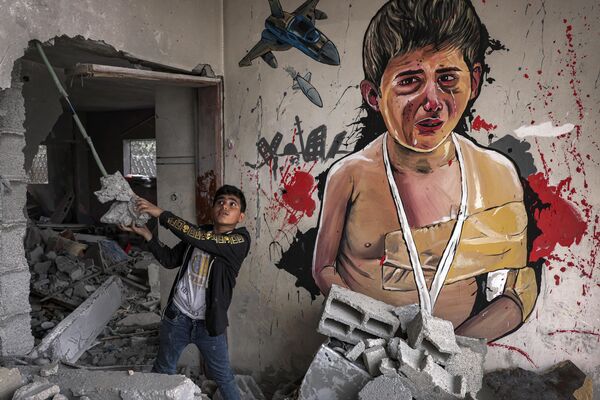 طفل فلسطيني يقف بجانب جدارية خلال معرض فني مختلط بعنوان &quot;الاحتلال يقتل الطفولة&quot; يقام وسط أنقاض المنازل التي دمرتها الغارات الجوية الإسرائيلية خلال التصعيد العسكري الأخير في مايو 2023 في دير البلح، وسط قطاع غزة في 8 يونيو 2023 . - سبوتنيك عربي
