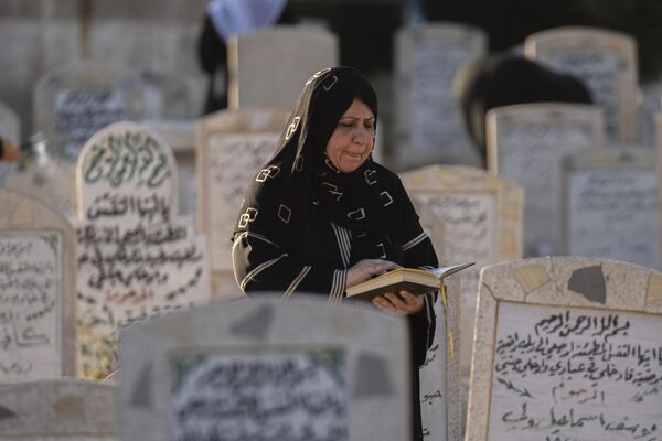 سيدة عراقية تقرأ القرآن على قبر أحد أقربائها، خلال اليوم الأول من عيد الأضحى المبارك، في مقبرة الغزالي في بغداد، العراق، 28 يونيو2023. - سبوتنيك عربي