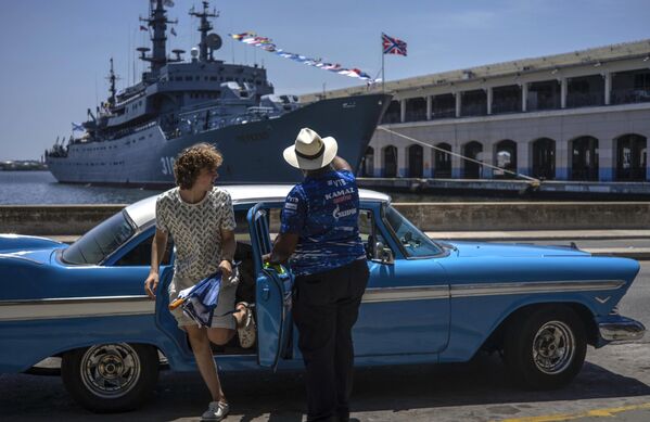 سائح يخرج من سيارة أمريكية كلاسيكية أمام سفينة التدريب التابعة للبحرية الروسية بيريكوب في خليج هافانا، كوبا 11 يوليو 2023. - سبوتنيك عربي