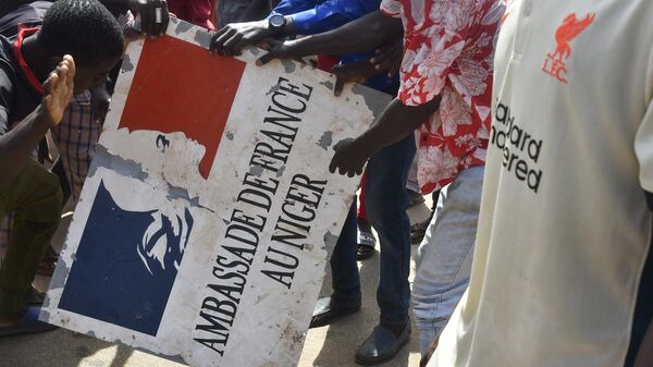 متظاهرون يحملون لافتة مأخوذة من السفارة الفرنسية في نيامي خلال مظاهرة أعقبت مسيرة لدعم المجلس العسكري في النيجر، 30 يوليو/ تموز 2023 - سبوتنيك عربي