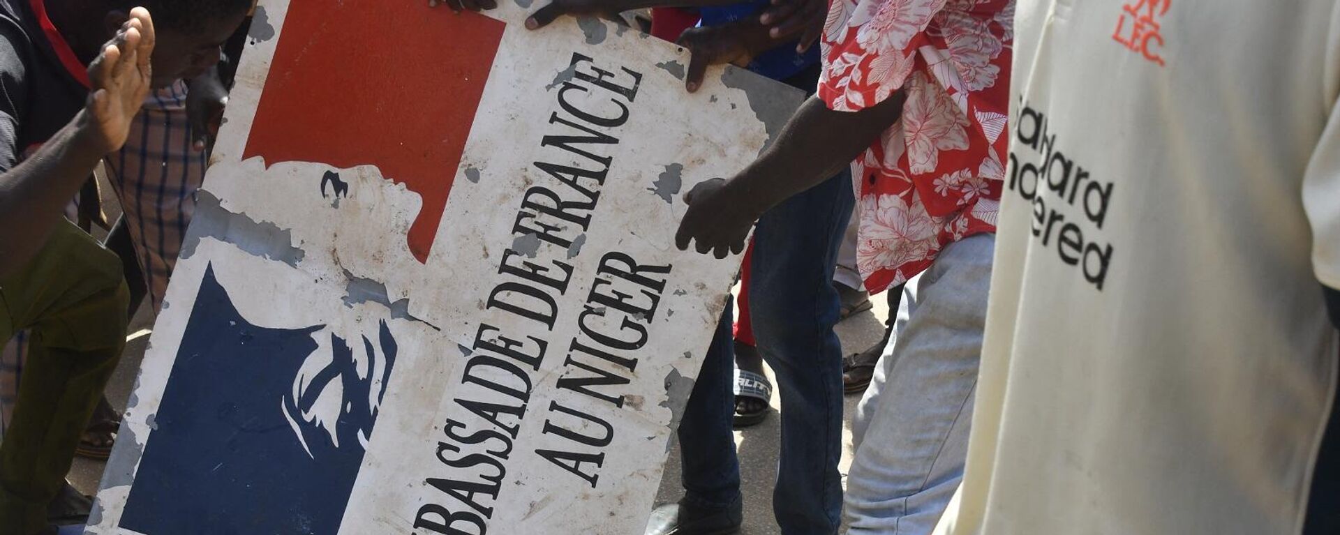 متظاهرون يحملون لافتة مأخوذة من السفارة الفرنسية في نيامي خلال مظاهرة أعقبت مسيرة لدعم المجلس العسكري في النيجر، 30 يوليو/ تموز 2023 - سبوتنيك عربي, 1920, 13.12.2023