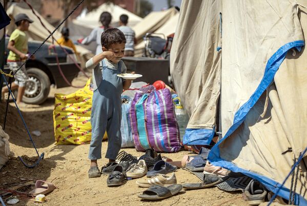 صبي صغير يتناول وجبته أمام خيمة في مخيم مؤقت أقيم للناجين من الزلزال في أمزميز في سلسلة جبال الأطلس الكبير في المغرب في 14 سبتمبر 2023. - سبوتنيك عربي