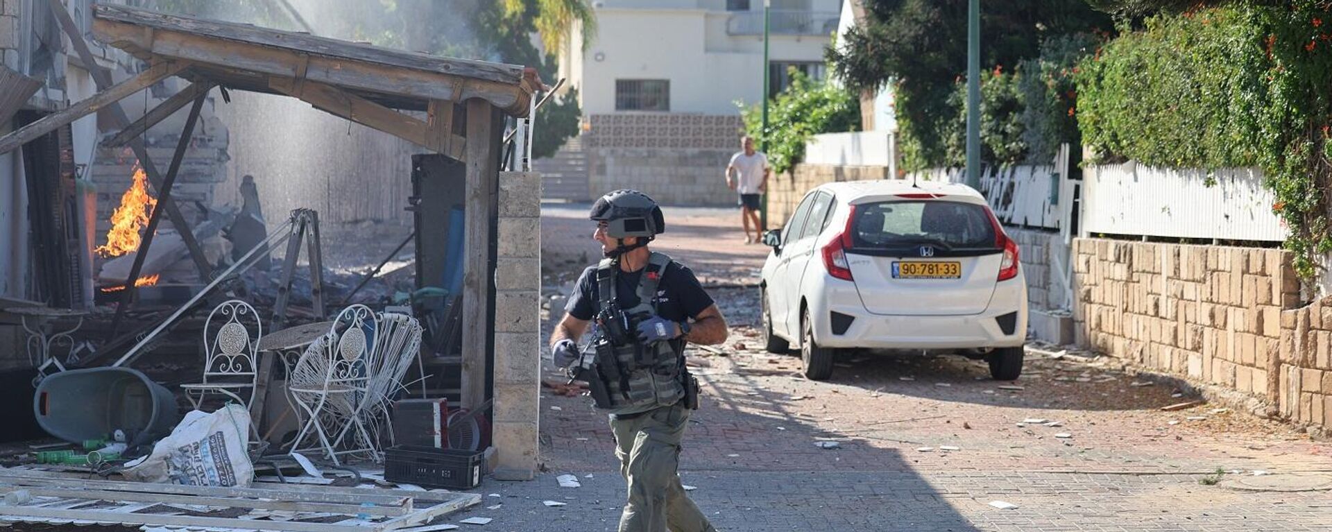 أحد أفراد القوات الإسرائيلية يمر أمام حريق مشتعل في منزل في عسقلان، في أعقاب هجوم صاروخي من قطاع غزة على جنوب إسرائيل، 7 أكتوبر/ تشرين الأول 2023 - سبوتنيك عربي, 1920, 04.01.2024