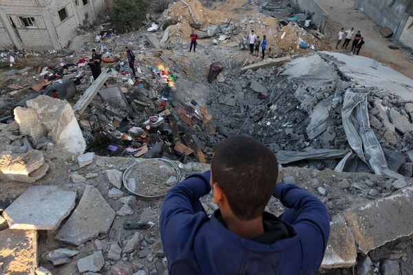صبي صغير ينظر بينما يقوم الناس بفحص أنقاض مبنى دمر جراء قصف إسرائيلي في رفح جنوب قطاع غزة، 21 أكتوبر 2023. - سبوتنيك عربي