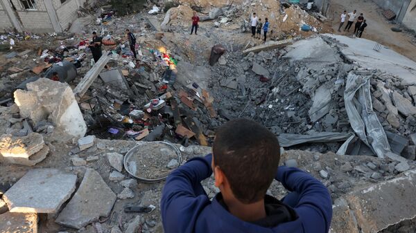 صبي صغير ينظر بينما يقوم الناس بفحص أنقاض مبنى دمر في قصف إسرائيلي في رفح جنوب قطاع غزة، 21 أكتوبر 2023. - سبوتنيك عربي