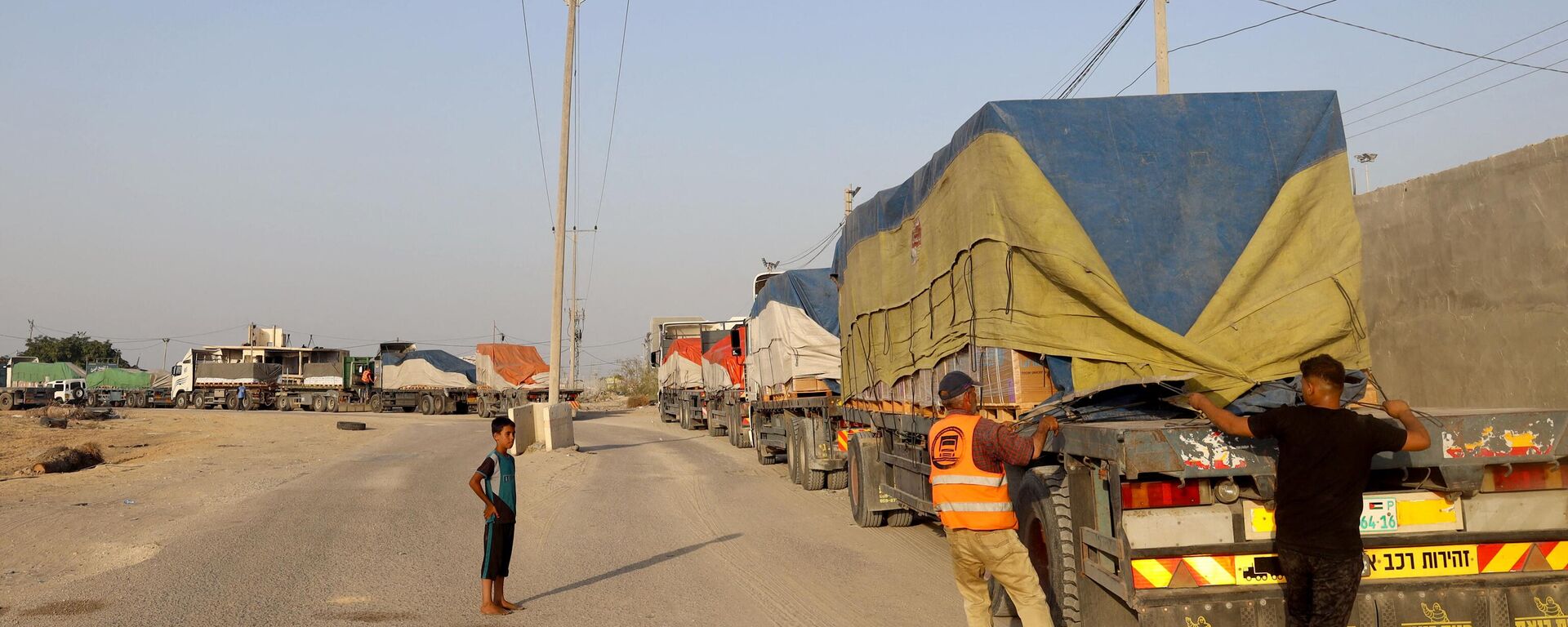 أشخاص يفرغون مساعدات إنسانية على قافلة شاحنات تدخل قطاع غزة من مصر عبر معبر رفح الحدودي في 21 أكتوبر 2023. - سبوتنيك عربي, 1920, 14.03.2024