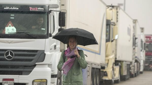 مراسلة تحمل مظلة على خلفية الشاحنات التي تحمل مساعدات إنسانية لعبور ميناء رفح المصري في طريقها إلى قطاع غزة، 27 نوفمبر 2023. - سبوتنيك عربي