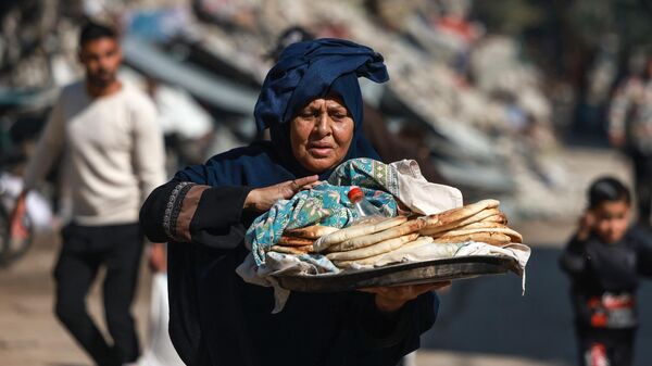 امرأة فلسطينية تحمل الخبز خارج مدرسة تابعة للأمم المتحدة في البريج بوسط قطاع غزة في 21 نوفمبر 2023، وسط المعارك المستمرة بين إسرائيل وحركة حماس الفلسطينية. - سبوتنيك عربي