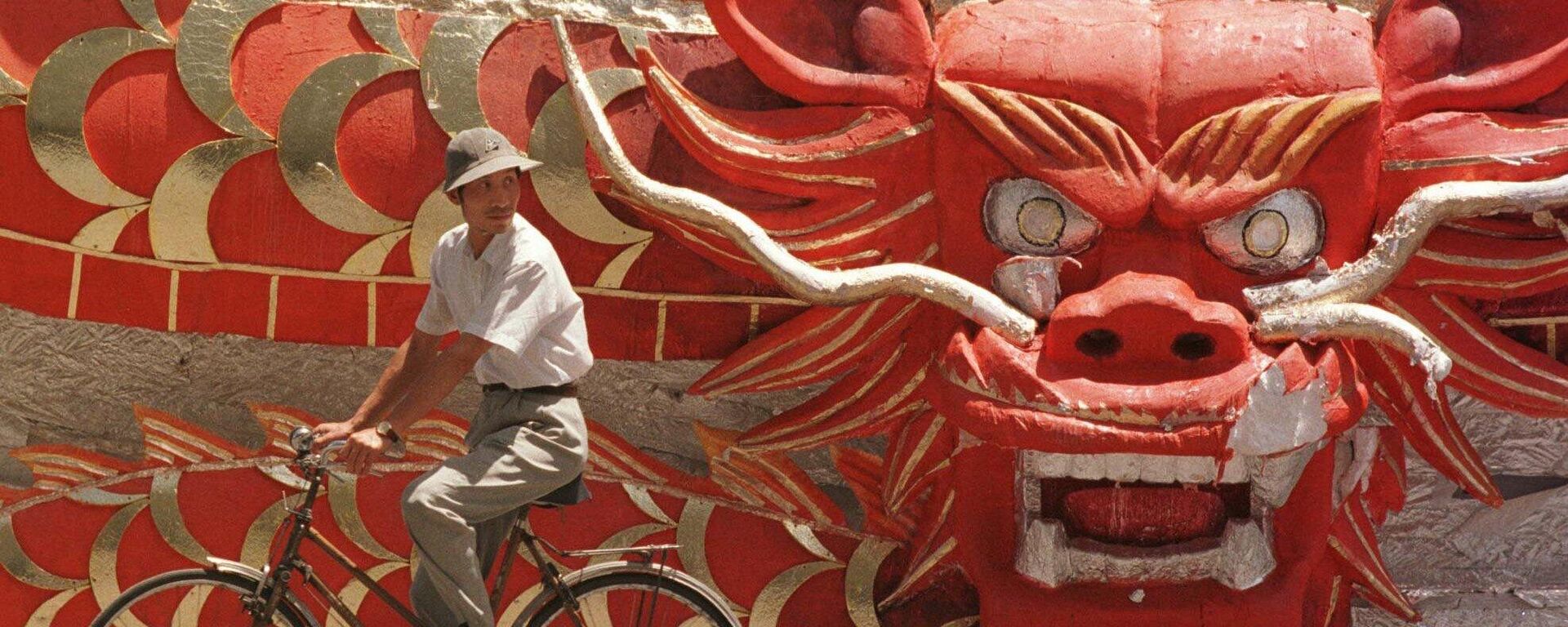 رجل صيني يمر بالدراجة بجوار مجسم عليه رأس تنين تم استخدامه خلال أحدى العروض للاحتفال باستعادة هونغ كونغ، المشهد خارج استاد العمال في بكين يوم الجمعة 4 يوليو 1997. - سبوتنيك عربي, 1920, 09.01.2024