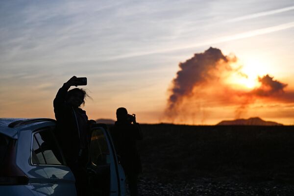 أشخاص يقفون بجوار سيارتهم بالقرب من كيفلافيك، أيسلندا، يلتقطون الصور مع تصاعد أعمدة الدخان أثناء ثوران بركاني بالقرب من غريندافيك، في 14 يناير 2024. - سبوتنيك عربي