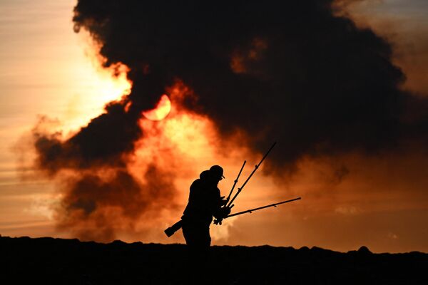 رجل يقوم بتعديل معدات التصوير الفوتوغرافي الخاصة به بالقرب من كيفلافيك، أيسلندا، مع تصاعد أعمدة الدخان أثناء ثوران بركاني بالقرب من غريندافيك، في 14 يناير 2024. - سبوتنيك عربي