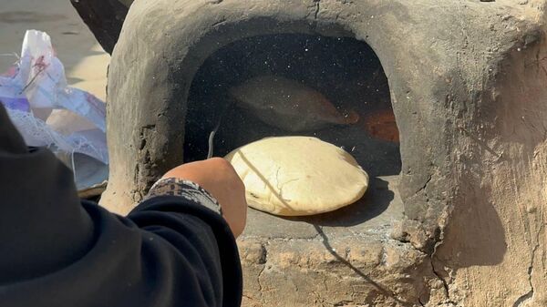 A displaced Palestinian makes bread on an old clay oven to feed her family and help the displaced - Sputnik Arabic