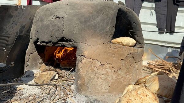 A displaced Palestinian makes bread on an old clay oven to feed her family and help the displaced - Sputnik Arabic