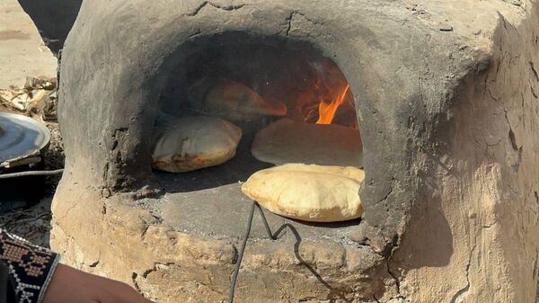 A displaced Palestinian makes bread on an old clay oven to feed her family and help the displaced - Sputnik Arabic