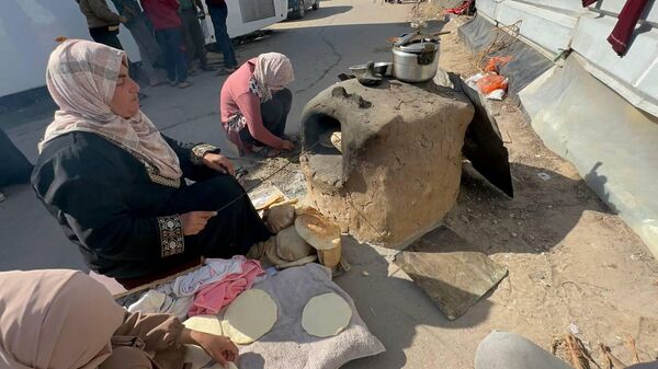 A displaced Palestinian makes bread on an old clay oven to feed her family and help the displaced - Sputnik Arabic