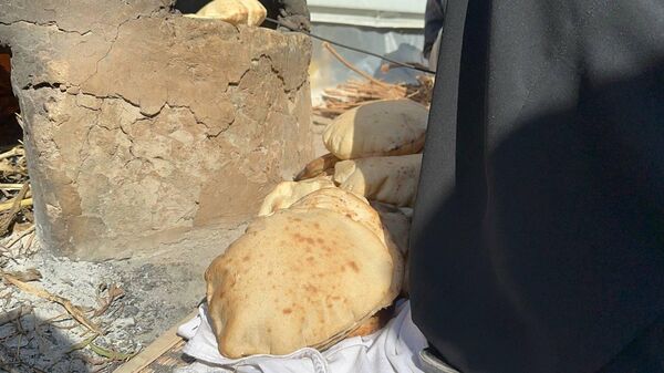 A displaced Palestinian makes bread on an old clay oven to feed her family and help the displaced - Sputnik Arabic