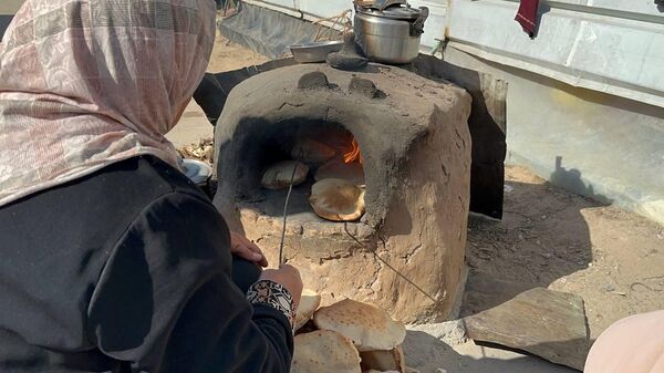 A displaced Palestinian makes bread on an old clay oven to feed her family and help the displaced - Sputnik Arabic