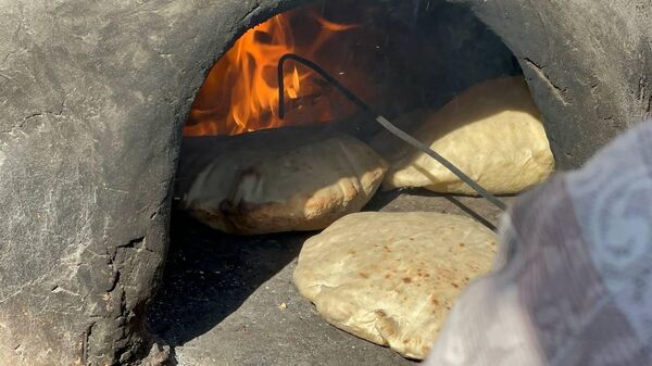 A displaced Palestinian makes bread on an old clay oven to feed her family and help the displaced - Sputnik Arabic
