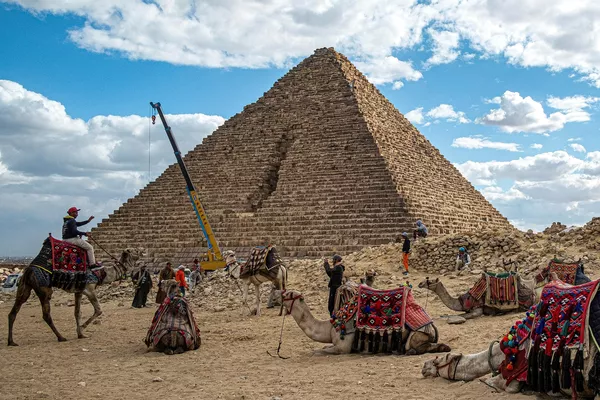 صورة لرافعة ترفع أحجار الغرانيت من أجل تثبيتها على الهرم، ويظهر أيضا قطيع من الجمال يأخذ قسطا من الراحة على الأرض أمام الهرم