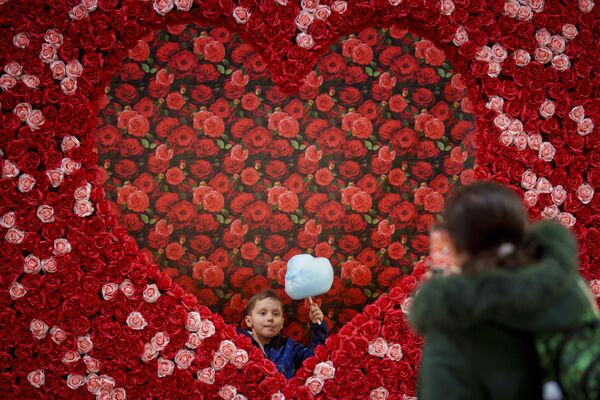طفل يحمل حلوى القطن أثناء الوقوف مع والدته أمام قلب خلال حدث عيد الحب في بوخارست، رومانيا، الثلاثاء 13 فبراير 2024. - سبوتنيك عربي