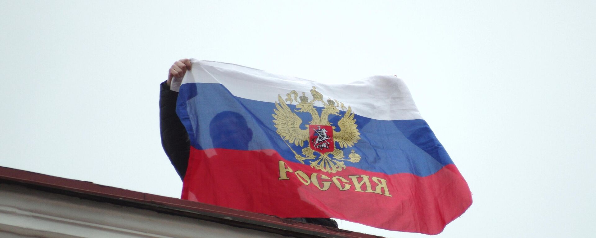 أحد السكان المحليين يحمل العلم الروسي على سطح مجلس مدينة سيفاستوبول. - سبوتنيك عربي, 1920, 19.03.2024