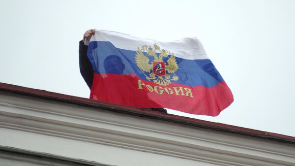أحد السكان المحليين يحمل العلم الروسي على سطح مجلس مدينة سيفاستوبول. - سبوتنيك عربي
