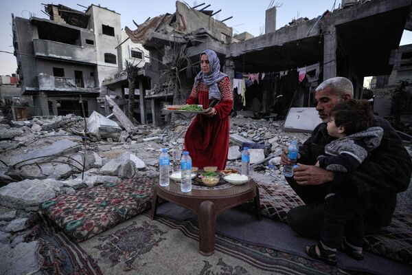 عائلة &quot;الناجي&quot; الفلسطينية، تتناول وجبة الإفطار وسط أنقاض منزلها، في أول أيام شهر رمضان، في دير البلح وسط قطاع غزة، فلسطين 11 مارس 2024. - سبوتنيك عربي