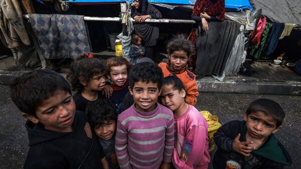 أطفال غزة -أطفال فلسطينيون نازحون يلتقطون صورًا أمام خيام مؤقتة في مخيم بجانب أحد شوارع رفح، قطاع غزة، فلسطين، في 14 مارس 2024 - سبوتنيك عربي