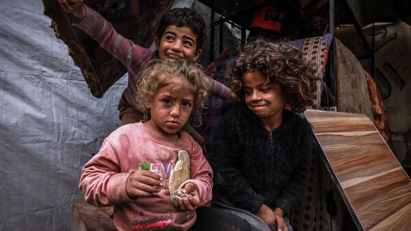 أطفال غزة - أطفال فلسطينيون نازحون يلتقطون صورًا أمام خيام مؤقتة في مخيم بجانب أحد شوارع رفح، قطاع غزة، فلسطين، في 14 مارس 2024 - سبوتنيك عربي