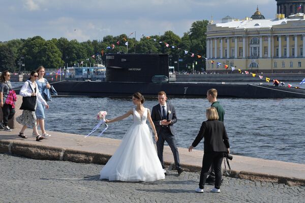 عروسان على جسر في مدينة سانت بطرسبورغ، في الخلفية الغواصة B-585&quot; سانت بطرسبورغ&quot;، التي تعمل بالديزل والكهرباء، في مياه نهر &quot;نيفا&quot; بعد التدريب على العرض البحري بمناسبة يوم البحرية الروسية. - سبوتنيك عربي