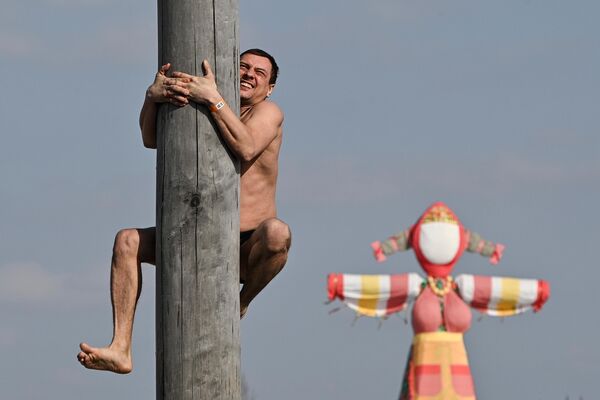 رجل يتسلق عمودًا أثناء احتفال محلي روسي في متحف حديقة إثنومير الإثنوغرافي في روسيا. - سبوتنيك عربي