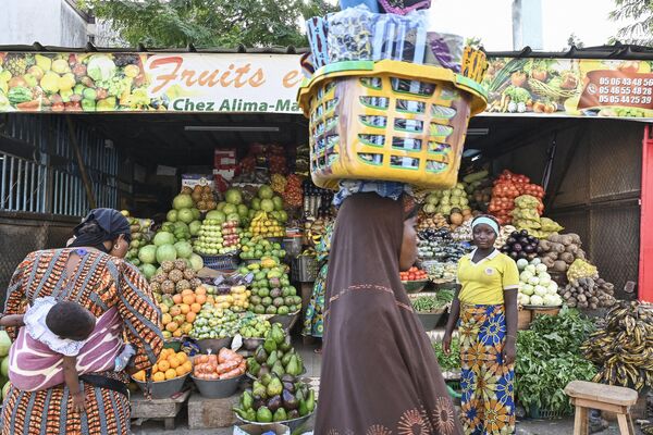 امرأة تحمل سلة غذائية على رأسها وهي تمر بجوار امرأة تبيع الفواكه والخضروات خلال شهر رمضان في أبيدجان، ساحل العاج، 25 مارس 2024. - سبوتنيك عربي