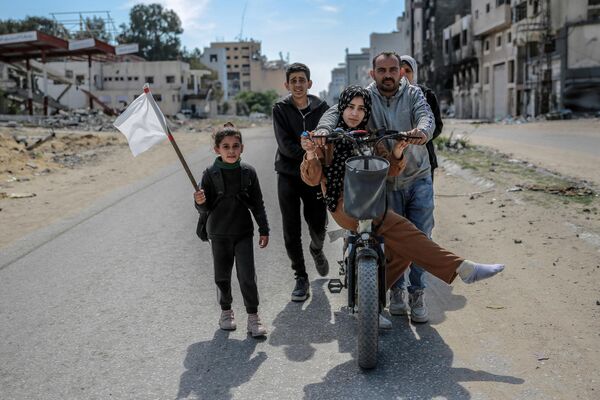 فتاة تحمل علمًا أبيض بينما تسير عائلة فلسطينية نازحة في مدينة غزة، في 25 مارس 2024، وسط الصراع المستمر بين إسرائيل وحركة &quot;حماس&quot; الفلسطينية. - سبوتنيك عربي