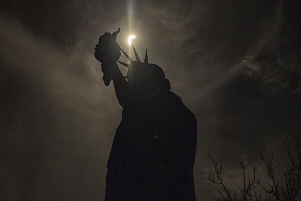 غطي القمر الشمس جزئيا خلف تمثال الحرية أثناء كسوف الشمس في جزيرة الحرية في نيويورك. - سبوتنيك عربي