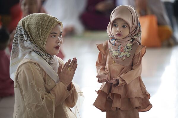 امرأة مسلمة توضح لابنتها كيفية الصلاة أثناء حضورهم الصلاة في المسجد الوطني لعيد الفطر، بمناسبة انتهاء شهر رمضان المبارك في كوالالمبور، ماليزيا، الأربعاء، 10 أبريل، 2024. - سبوتنيك عربي