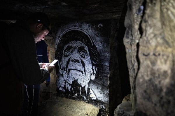 زائر ينظر إلى رسم على الجدران في سراديب الموتى المحرمة في باريس. - سبوتنيك عربي