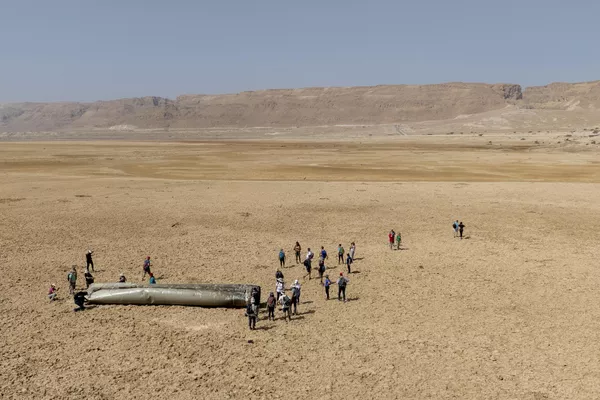 أشخاص يتجمعون حول أحد مكونات صاروخ بالستي تم اعتراضه وسقط بالقرب من البحر الميت في إسرائيل، السبت 20 أبريل 2024. - سبوتنيك عربي
