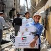 Мужчины идут сквозь завалы мимо поврежденных зданий с пакетами гуманитарной помощи - سبوتنيك عربي
