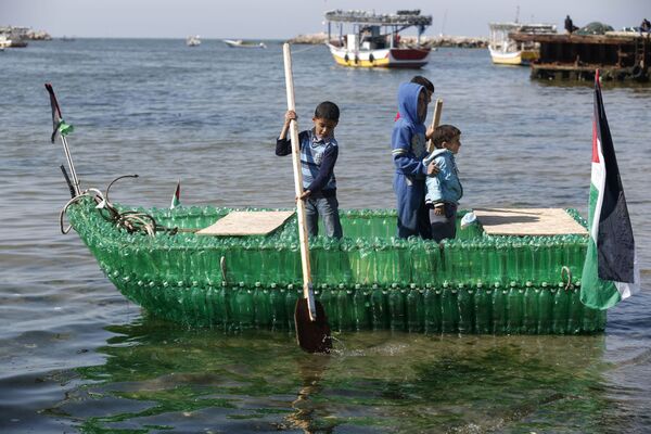أطفال فلسطينيون على متن قارب مصنوع من الزجاجات البلاستيكية في ميناء مدينة غزة - سبوتنيك عربي